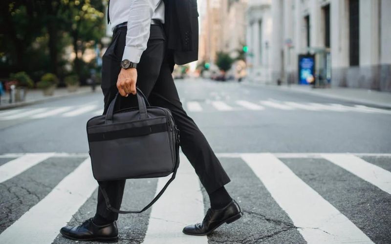 Homme habillé en costard, traverse un passage piéton, avec une sacoche d'ordinateur à la main.